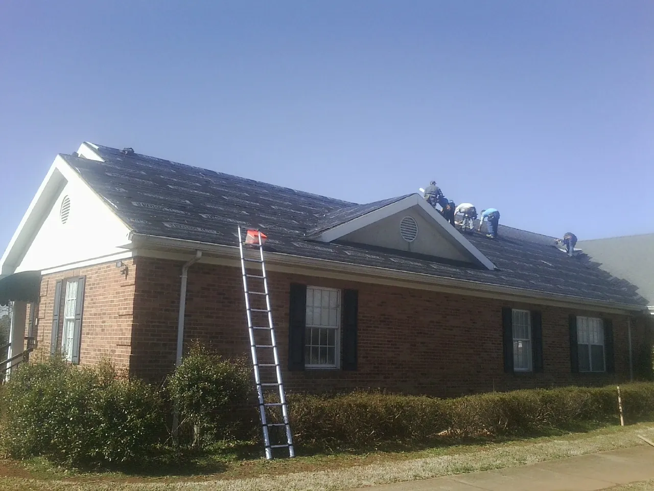 Crew tearing shingles off a brick ranch roof with a ladder set — Metal Roof Repair work by our crew in Island Park