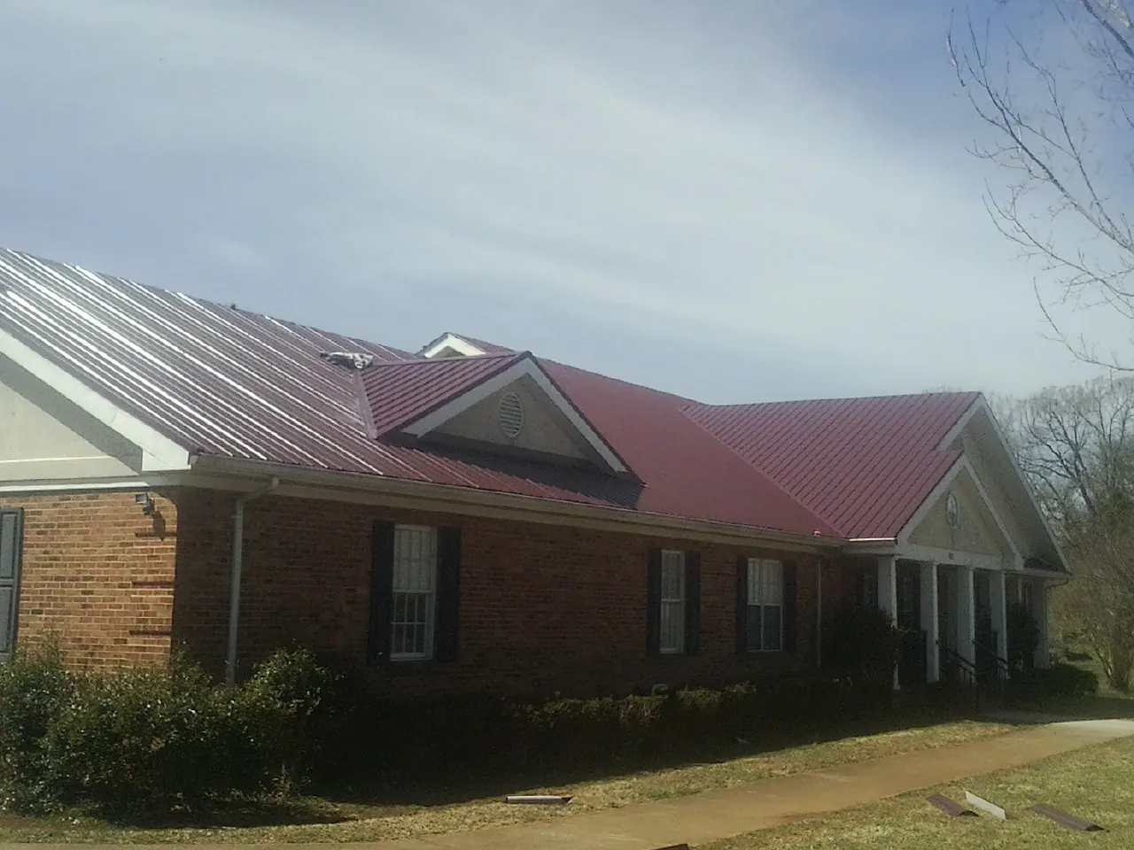 Red metal roof with gabled entries on a long brick building, from a Hail Damage Roof Repair job in Island Park
