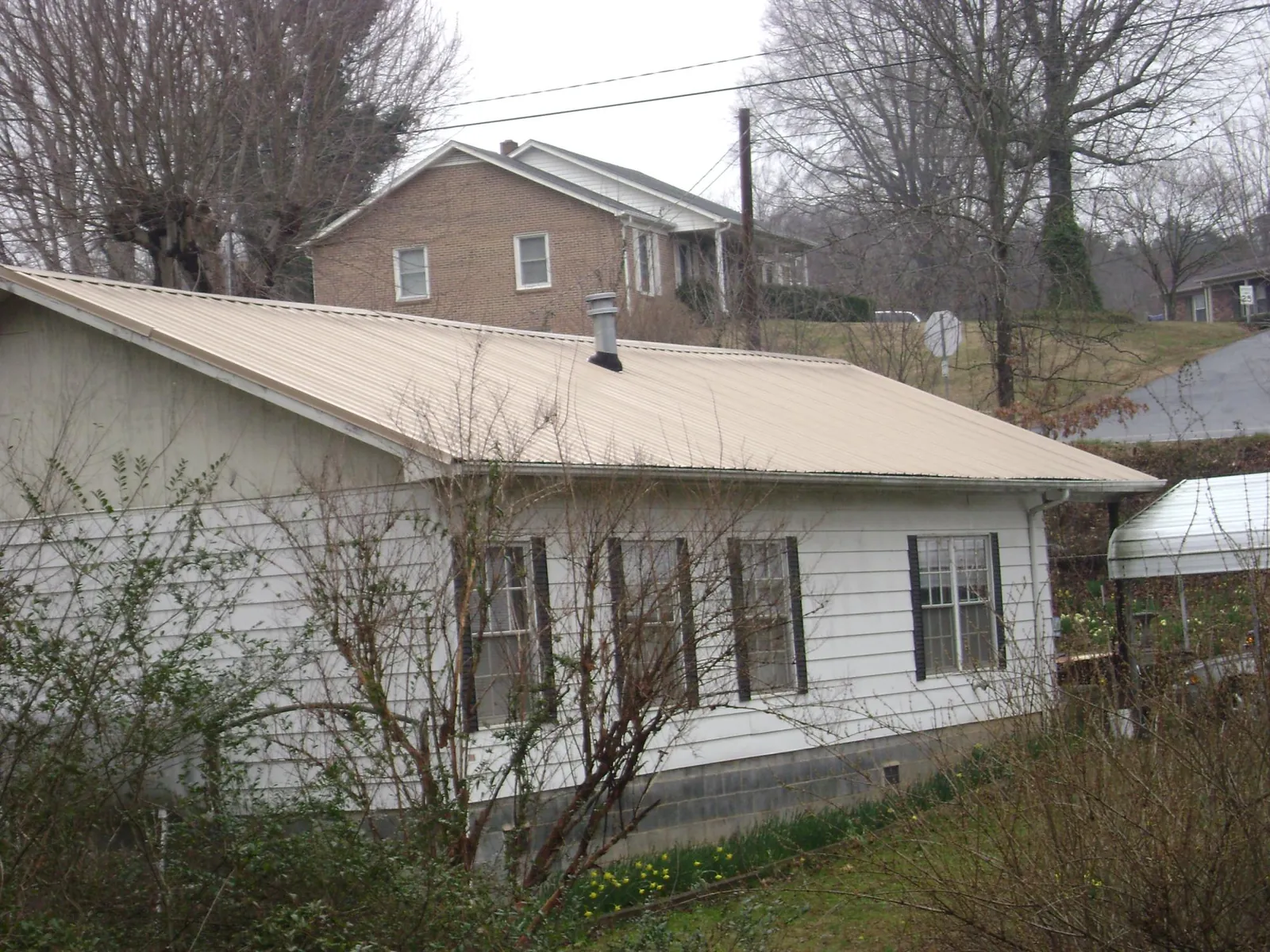 Tan metal roof on a white sided house set into a hillside — Commercial Roofing by Roofing Brothers in Island Park